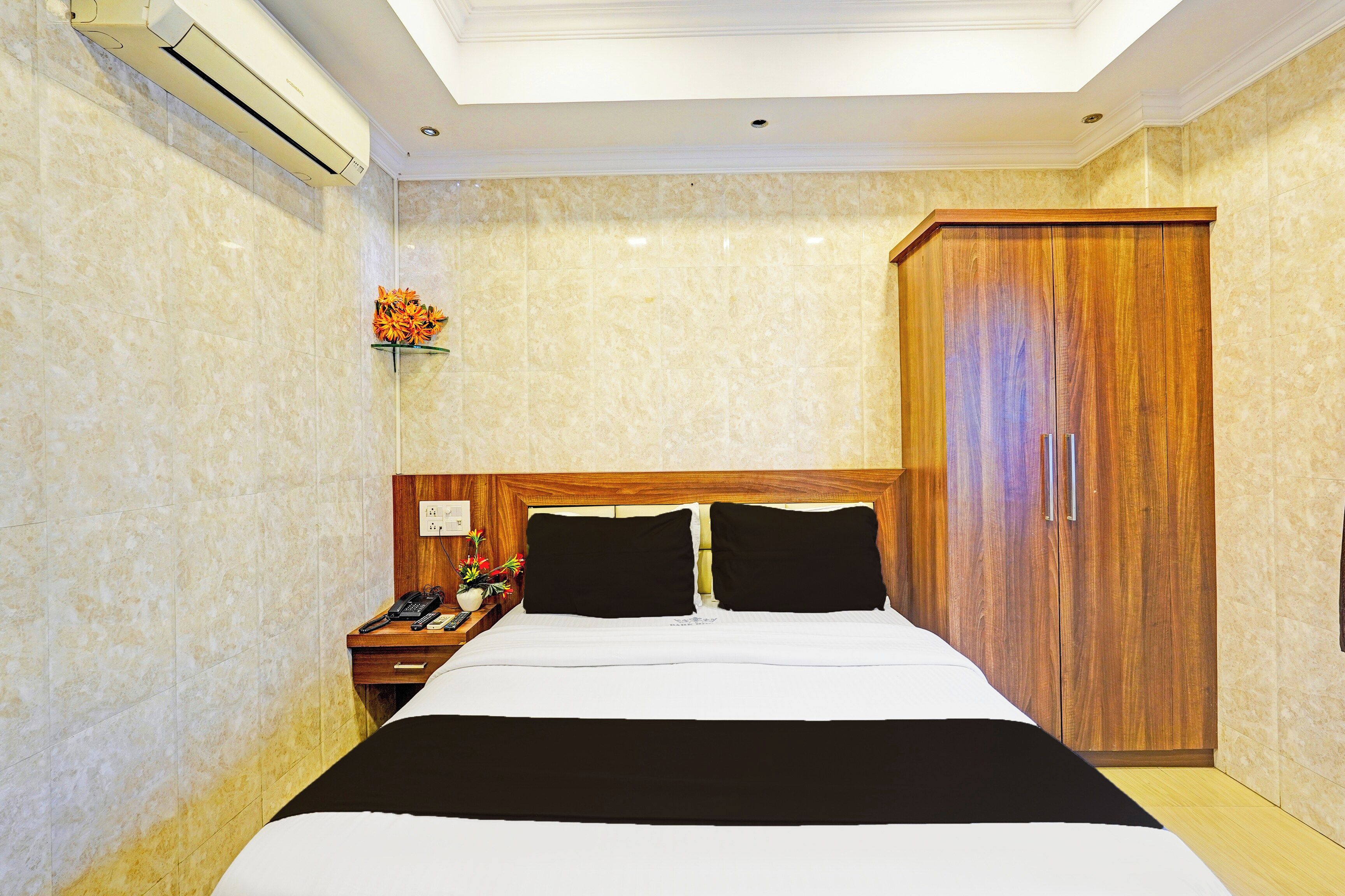 A hotel room with a bed, a nightstand, a telephone, a flower vase, and a wardrobe.