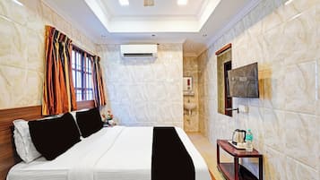 Habitación de hotel con cama, televisión montada en la pared, aire acondicionado y una mesita con una botella y una tetera.