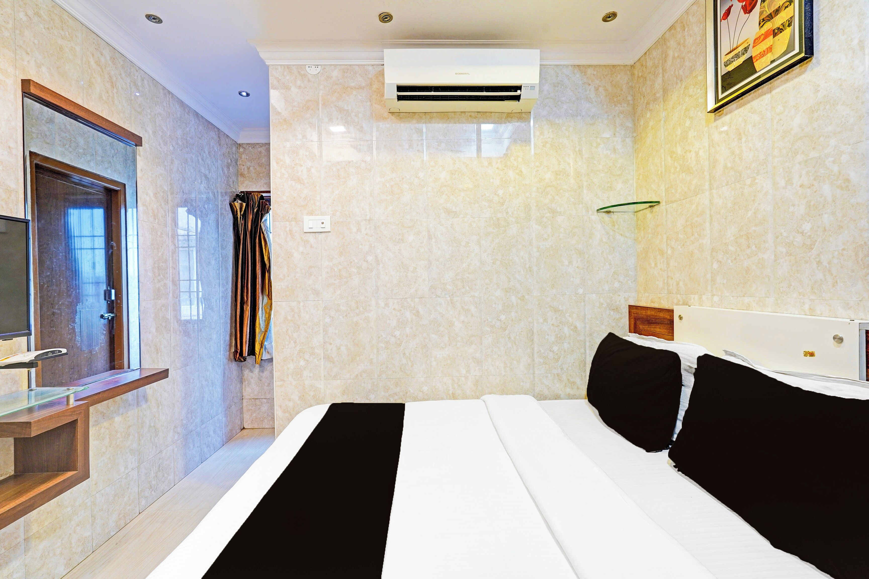 A hotel room with a bed, a TV, an air conditioning unit, and a bathroom with a shower curtain.
