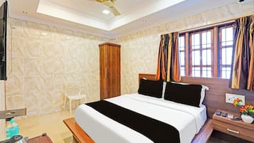 Habitación de hotel con cama, un armario de madera, una silla, una mesita de noche con teléfono y un florero, y una ventana con cortinas.
