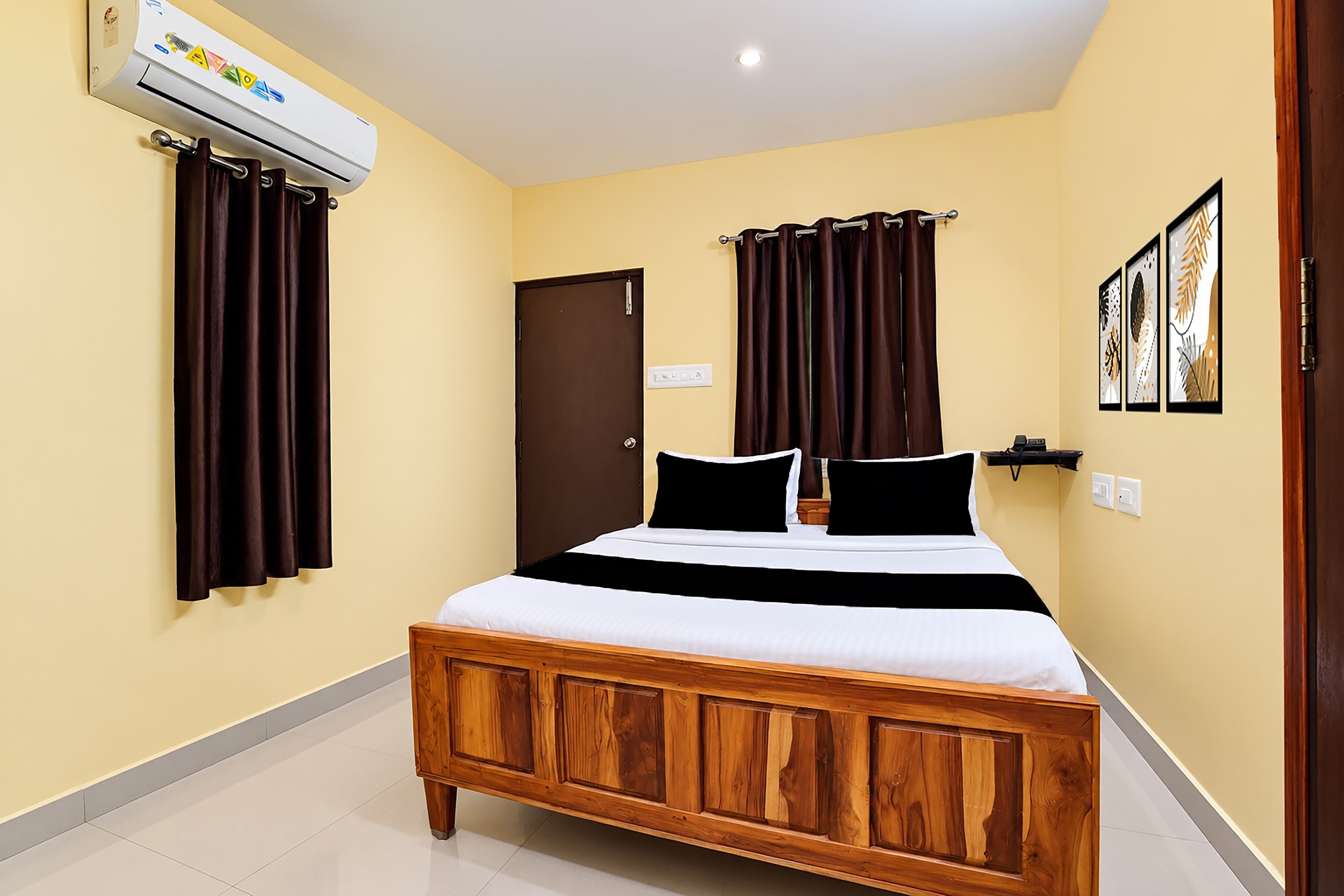 Quarto de hotel com cama de madeira, cortinas escuras, uma porta e ar condicionado fixado na parede.