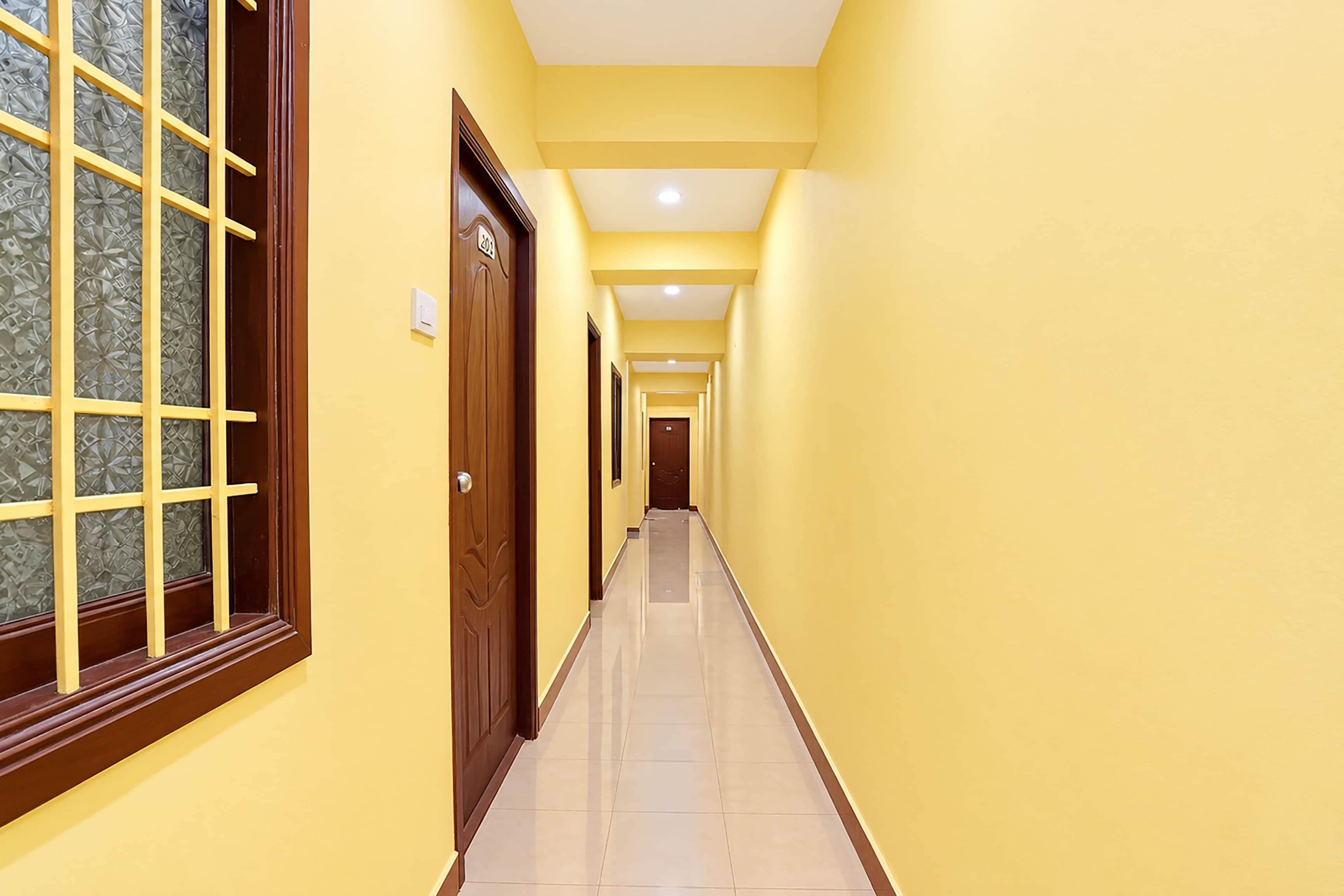 A long, narrow hallway with yellow walls and a tiled floor, leading to a door with a number plaque.
