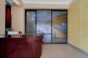 A reception area with a glass partition, a reception desk, a staircase, and a yellow textured wall. - Collection O KSRTC Bus Station Kottayam (Kottayam)