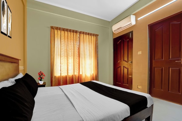 A hotel room with a bed, a nightstand with a vase of flowers, a window with curtains, and a door. - Collection O KSRTC Bus Station Kottayam (Kottayam)