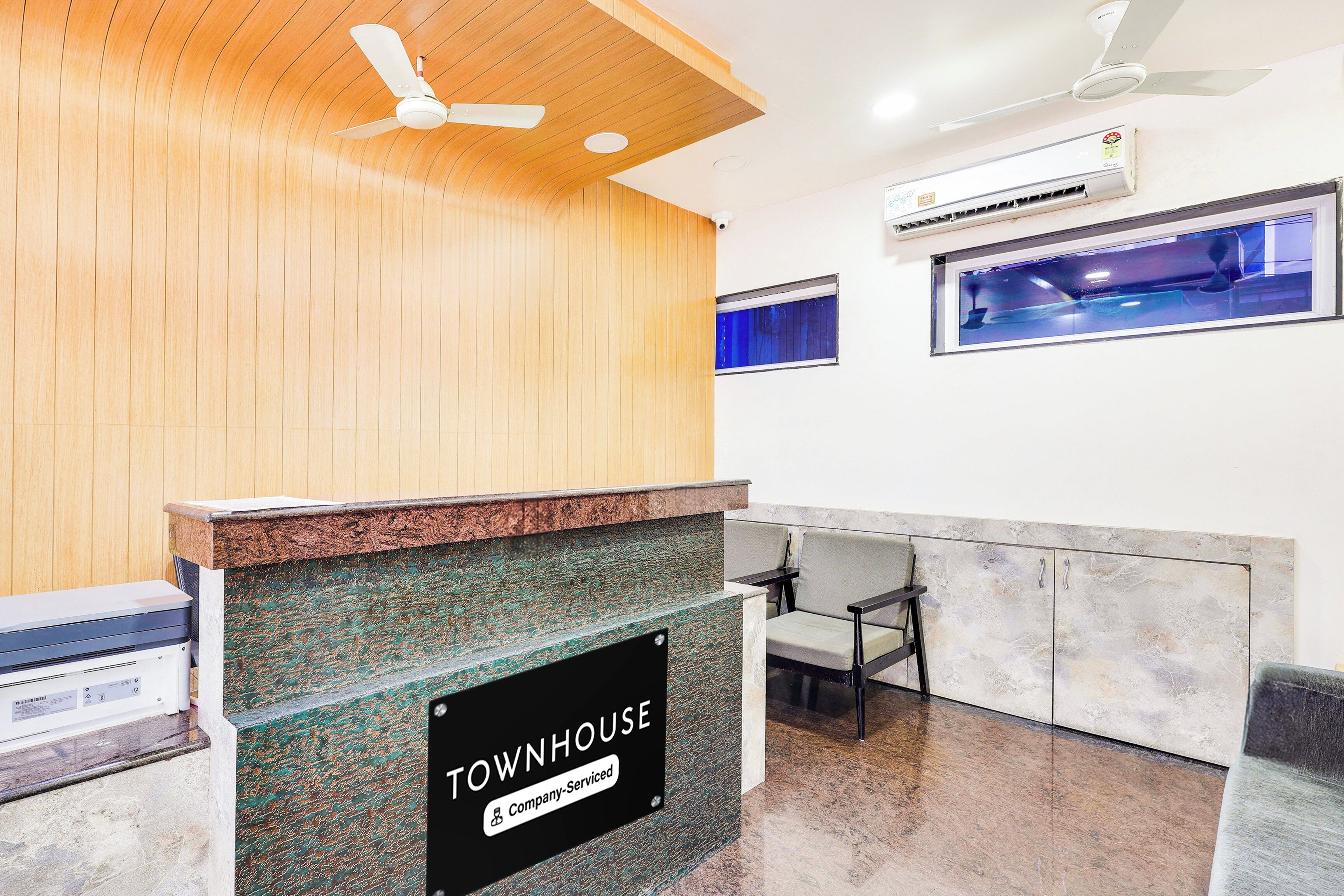 A reception area with a wooden ceiling, a sign reading 'TOWNHOUSE Company Serviced', a reception desk, and a seating area with a view of the street.