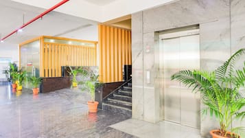 A modern lobby with a reception desk, a staircase, and an elevator.
