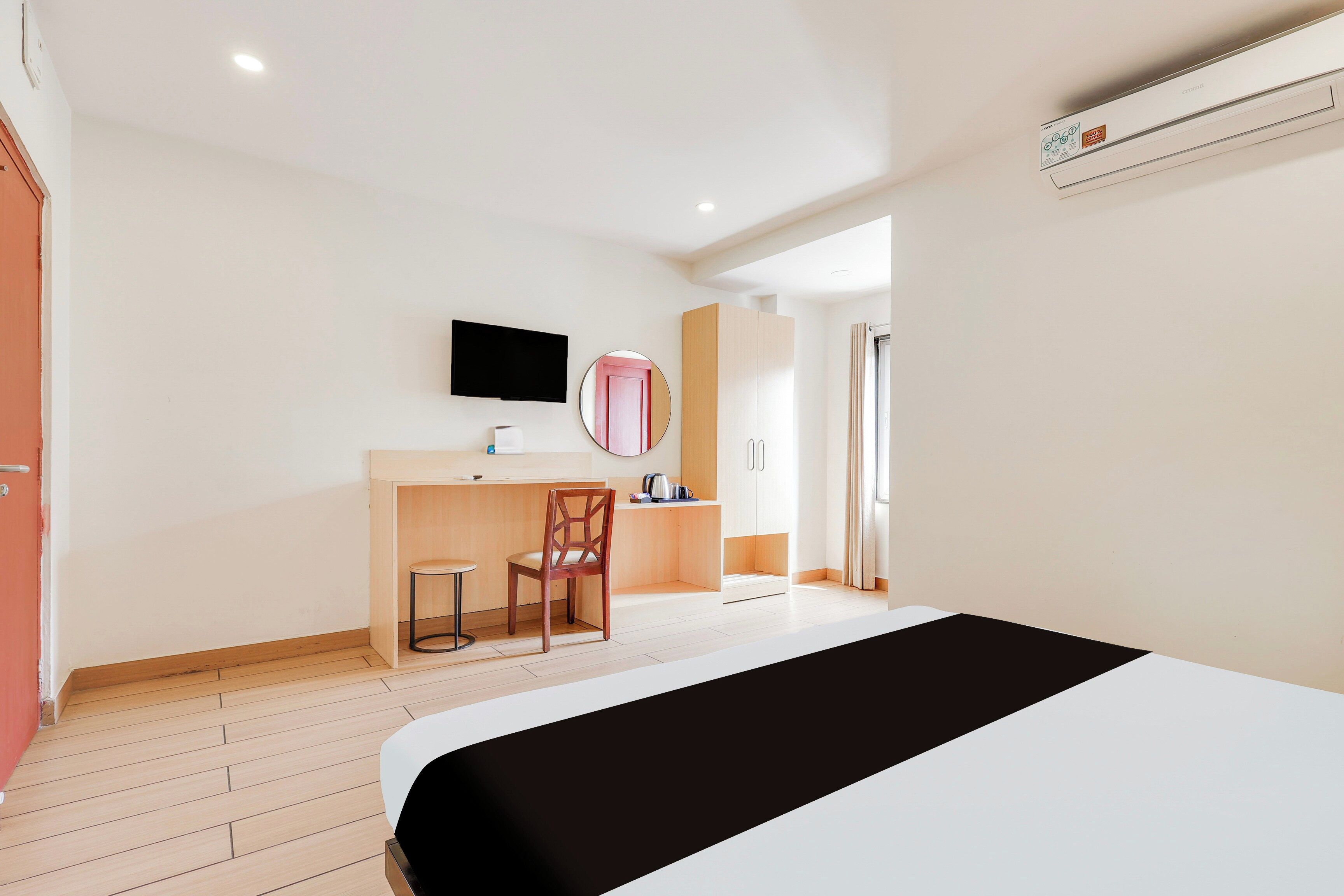 A hotel room with a bed, a desk with a chair, a television, a mirror, and a wardrobe.
