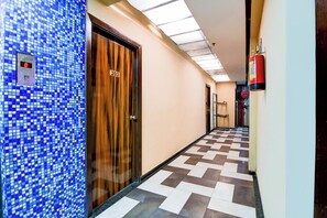 Um corredor com piso xadrez, porta de madeira com um número e extintor de incêndio.