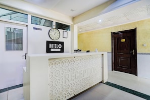 Una recepción de hotel con un reloj, un cartel que indica la hora de salida y una zona de recepción con una puerta etiquetada 'G1'.