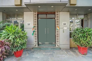 Entrada de un edificio con una puerta verde, dos macetas y un portón metálico decorativo.