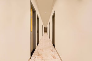 Pasillo de hotel con piso de mármol, puertas a ambos lados y techo con iluminación empotrada.