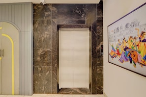 Un pasillo con la puerta cerrada de un ascensor, una cámara de seguridad y un mural colorido en la pared.