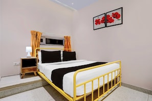 Un dormitorio con cama, cortinas, una mesita de noche con lámpara y un cuadro colgado en la pared.