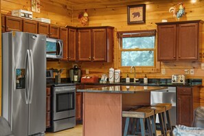 A kitchen with wooden cabinets, stainless steel appliances, a window, and a wooden island with stools. - Sleeps 14, Home Theater, Game Room, Hot Tub, Mountain Views (Gatlinburg)