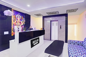 Ein Hotel-Rezeptionsbereich mit einer Rezeption, einem an der Wand befestigten Fernseher und einer Sitzecke.