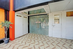 Entrada de hotel con piso de diseño geométrico, una planta en maceta y puerta de vidrio con letrero que indica 'PULL'.