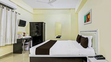 Habitación de hotel con cama, mesita de noche, escritorio con silla, armario, ventilador de techo, televisor y un cuadro en la pared.