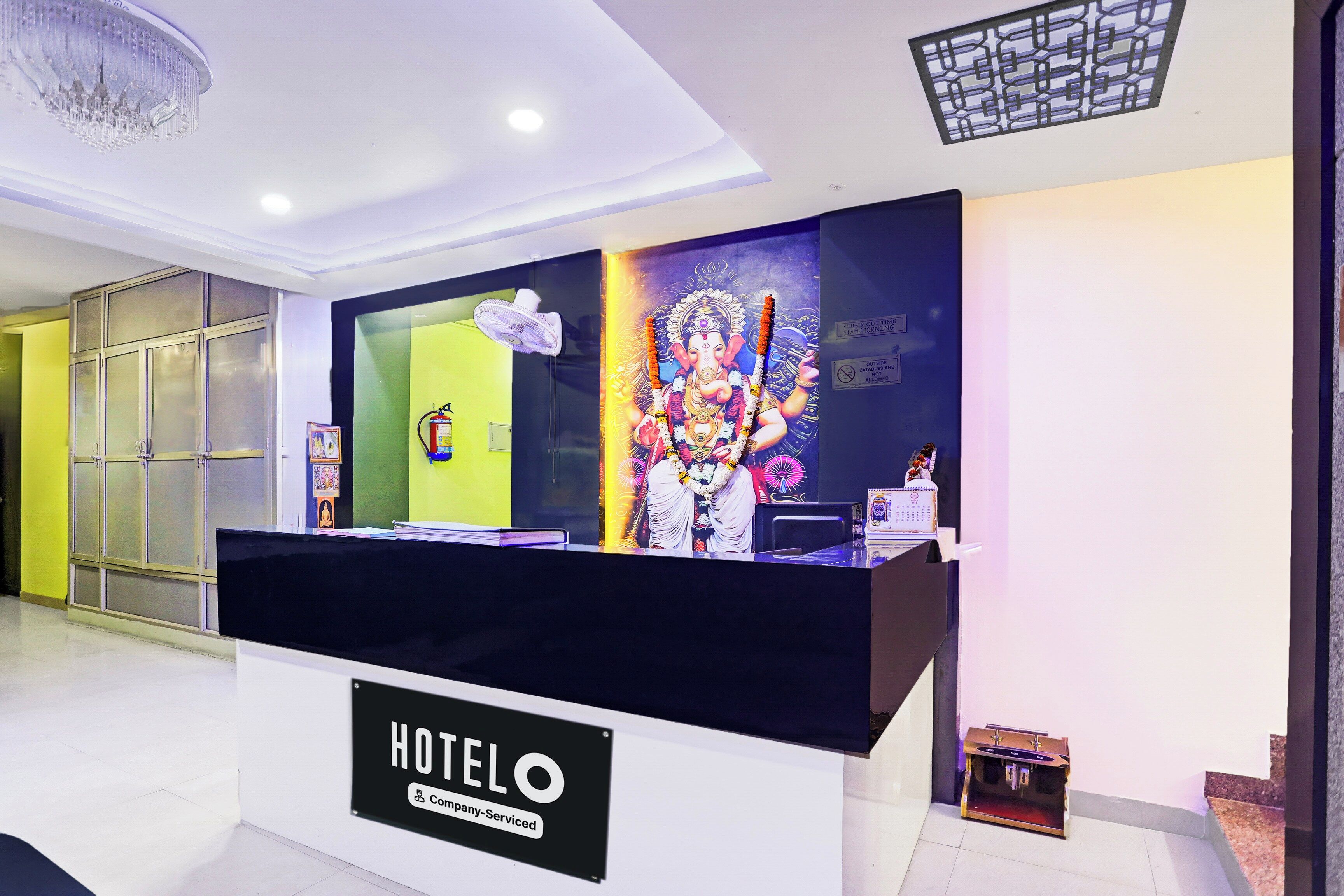A hotel reception desk with a 'HOTELO' sign, a wall-mounted fan, and a religious mural.