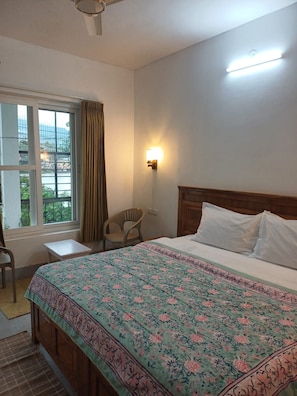 Habitació d'hotel amb un llit, una cadira, una taula petita, una finestra amb cortines i una làmpada penjada a la paret.