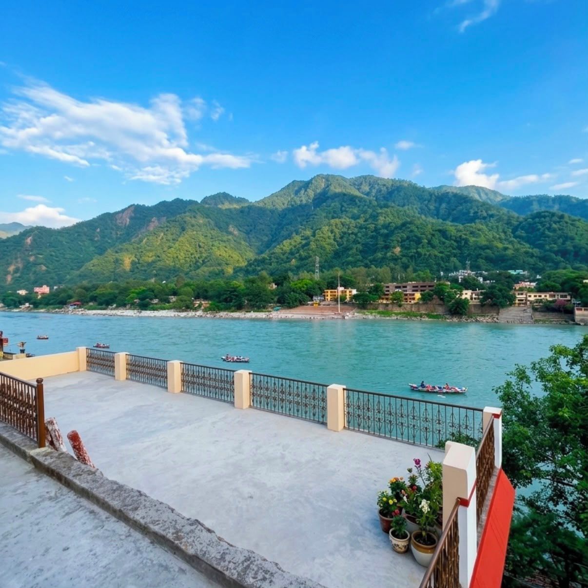 A riverside view with mountains in the background, a concrete deck with a railing, and potted plants.