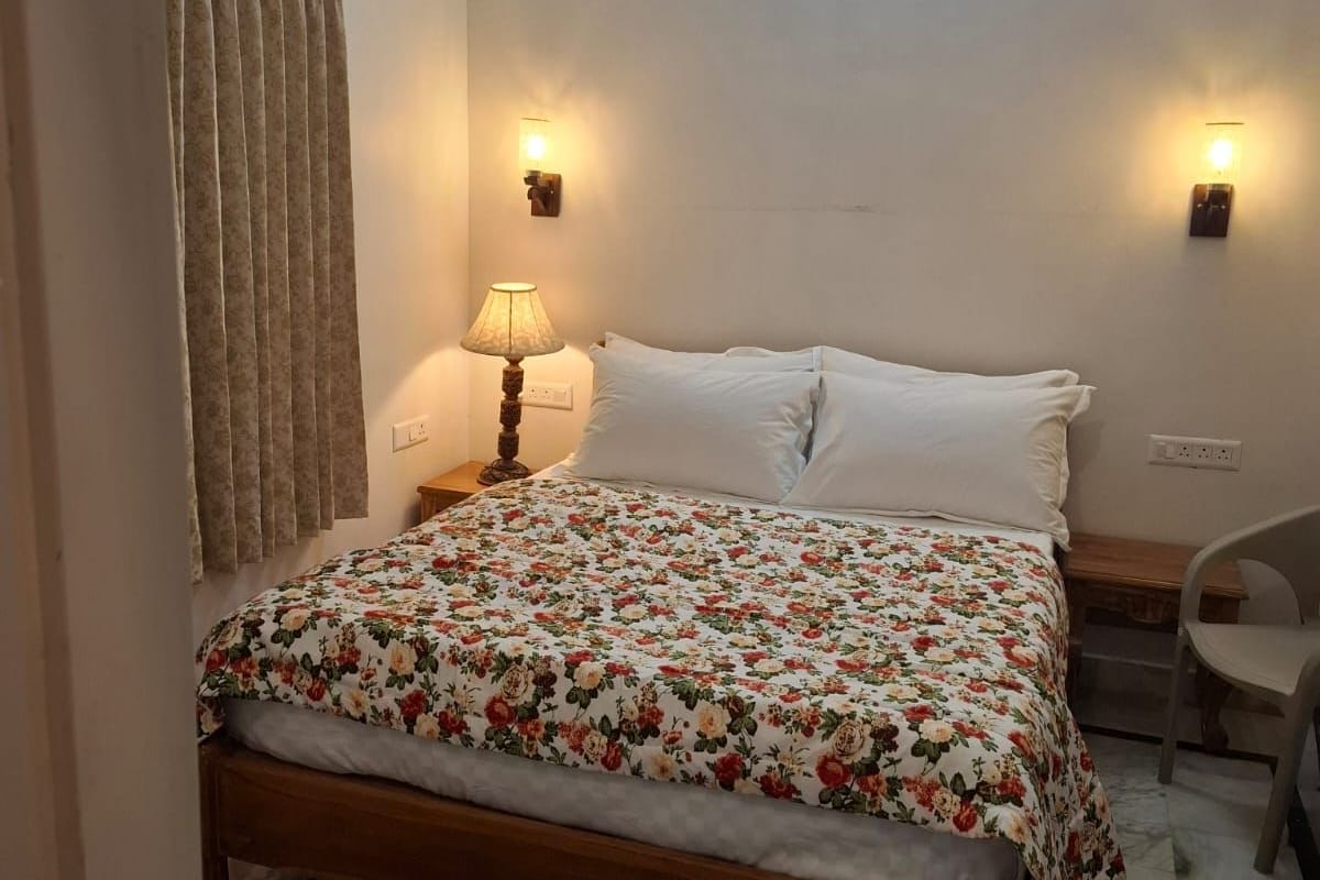 A bedroom with a bed, two wall-mounted lamps, a ceiling light, a chair, and a patterned rug.