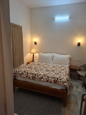 A bedroom with a bed, two wall-mounted lamps, a ceiling light, a chair, and a patterned rug. - AJASRA-GANGA (Rishikesh)