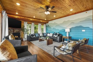 A cozy living room with a fireplace, leather sofas, a coffee table, and a mountain mural on the wall. - Sleeps 36, Private Indoor Pool, Theater, Arcade, Hot Tub, 11 Mi to Dollywood (Sevierville)