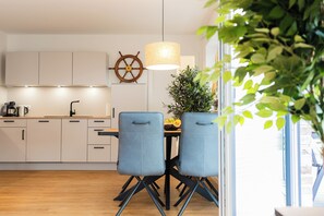 A modern kitchen with white cabinets, a coffee machine, and a ship's wheel decoration. - Yellow Duck - Beach Runner 4.4 | Sauna. Beach chair. Near the Baltic Sea. (Kellenhusen)