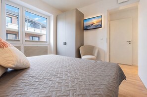 A bedroom with a bed, a chair, a wardrobe, and a TV on the wall. - Yellow Duck - Beach Runner 4.4 | Sauna. Beach chair. Near the Baltic Sea. (Kellenhusen)