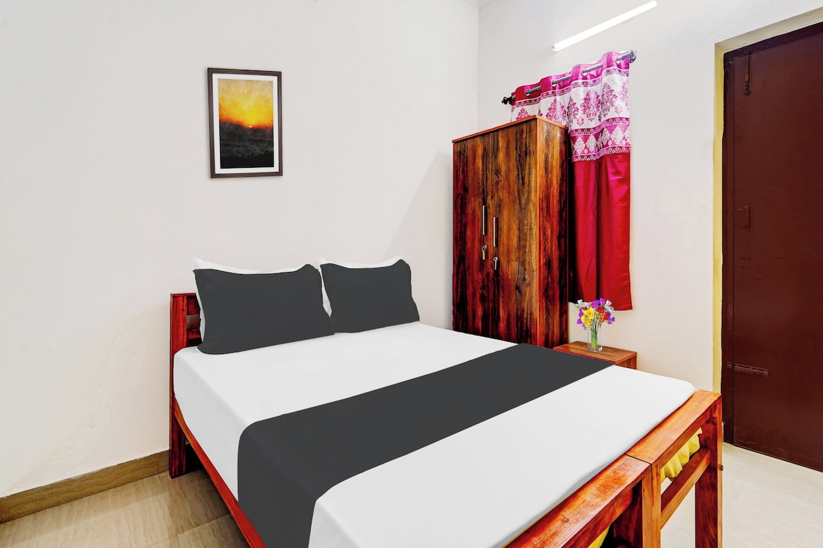 Una cama bien hecha con colcha blanco y negro, un cabecero de madera y una mesita de noche con un jarrón de flores.