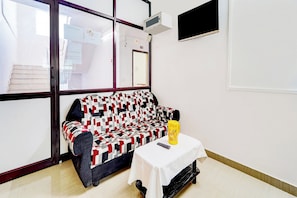Una habitación con un sofá estampado, una mesita con una botella amarilla y un televisor montado en la pared.