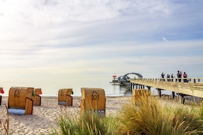 En strand med strandstolar som är numrerade, en brygga och en bro i bakgrunden.