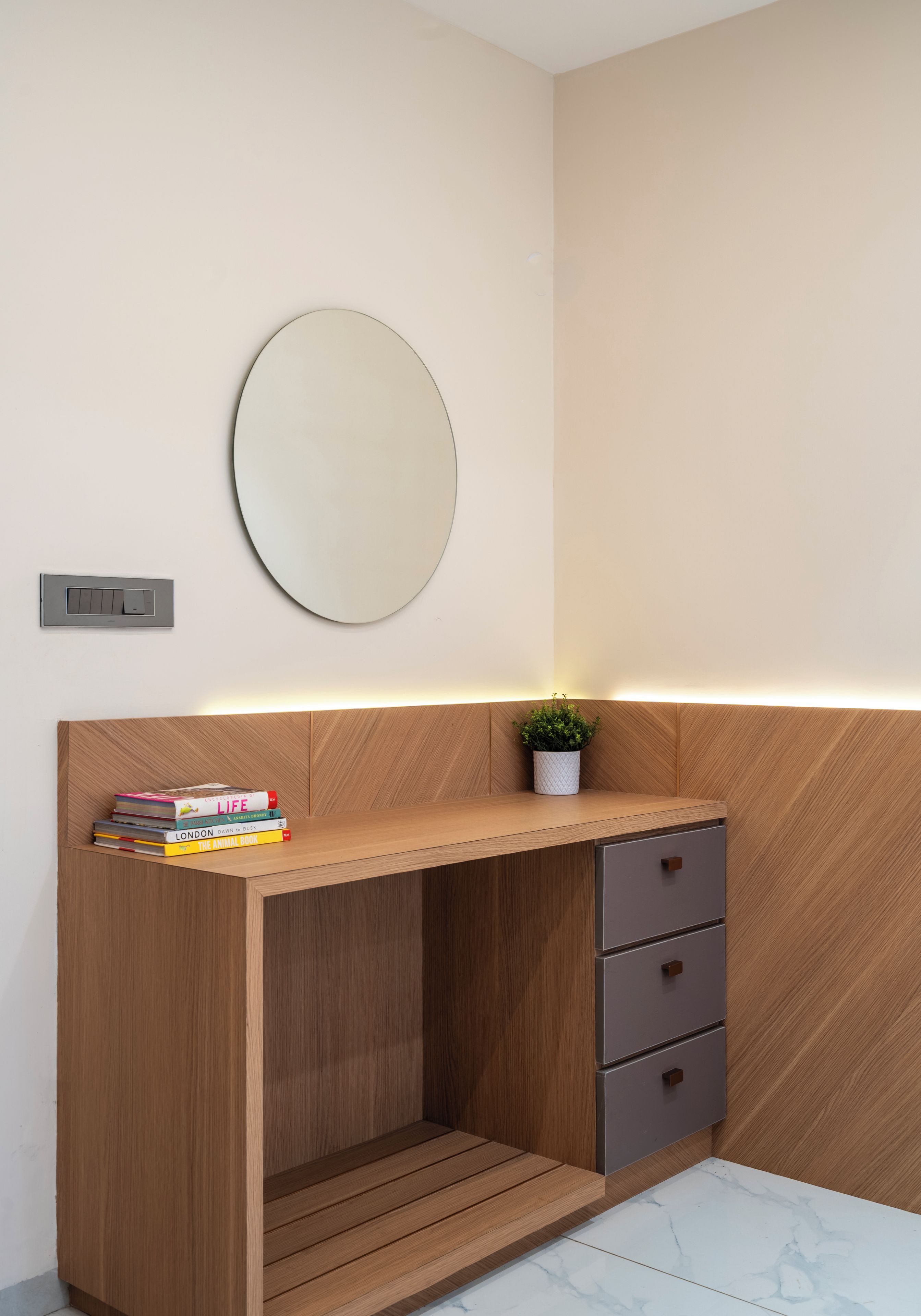 A modern bathroom with a wooden vanity, a round mirror, and a small potted plant.