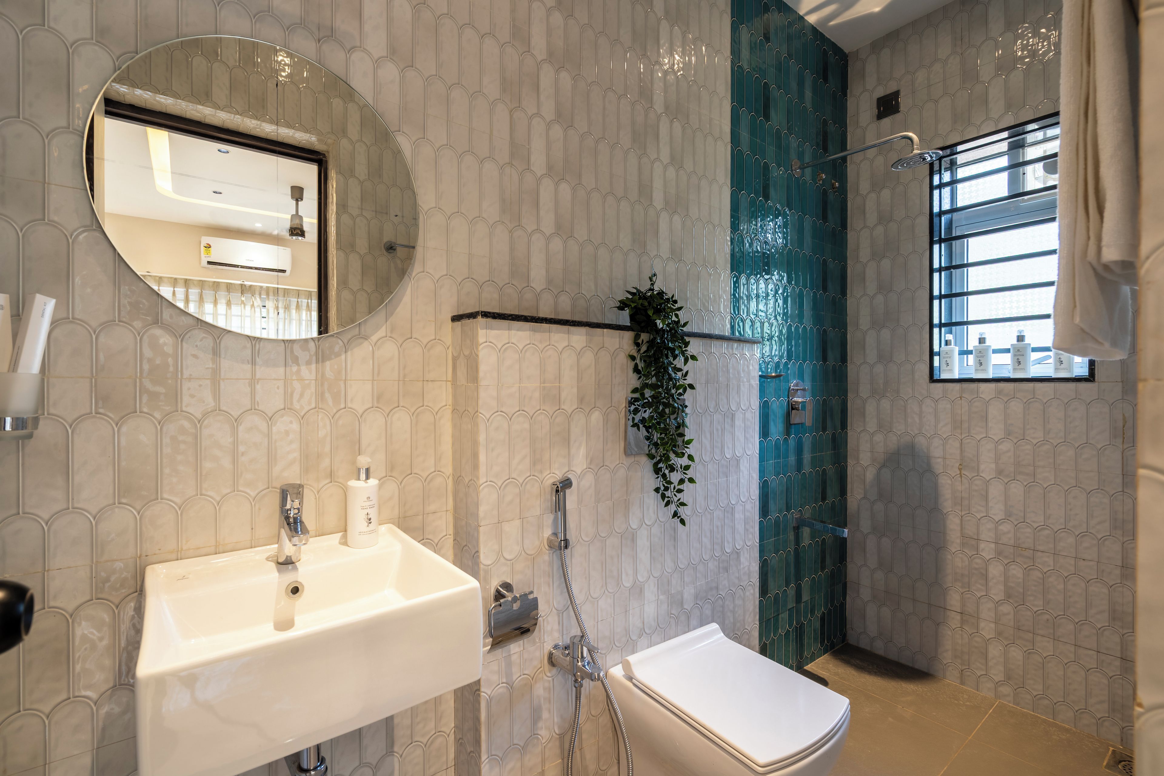 A bathroom with a white sink, a mirror, a shower with a glass door, and a window with blinds.