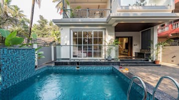 Un edificio residencial con piscina, un balcón con barandilla y plantas en macetas.
