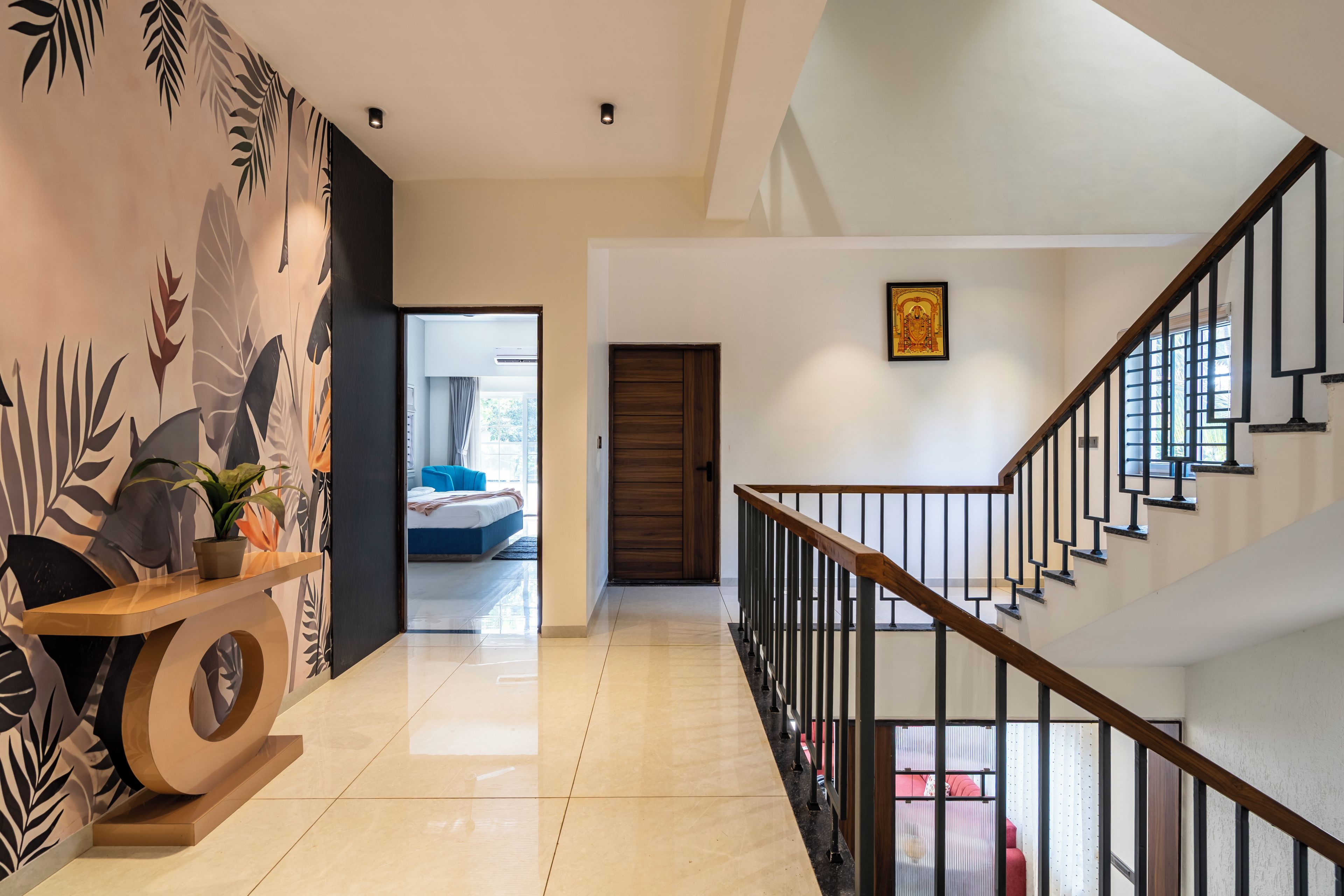 A hallway with a wooden floor, a staircase with a metal railing, and a door leading to a bedroom.