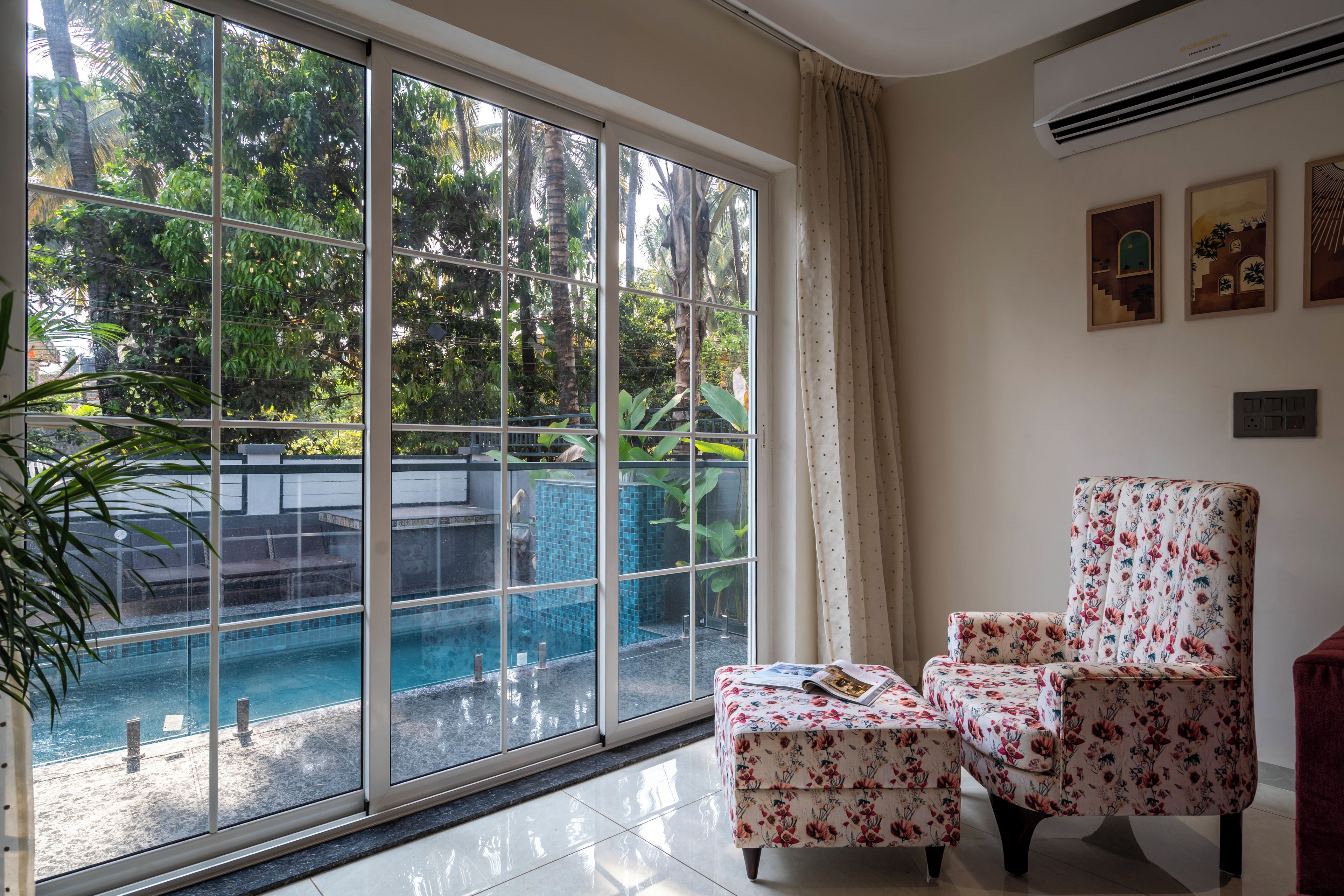 A room with a large sliding glass door leading to a pool area, a floral armchair, and a small table with a magazine.