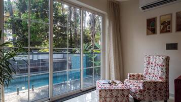 A room with a large sliding glass door leading to a pool area, a floral armchair, and a small table with a magazine.