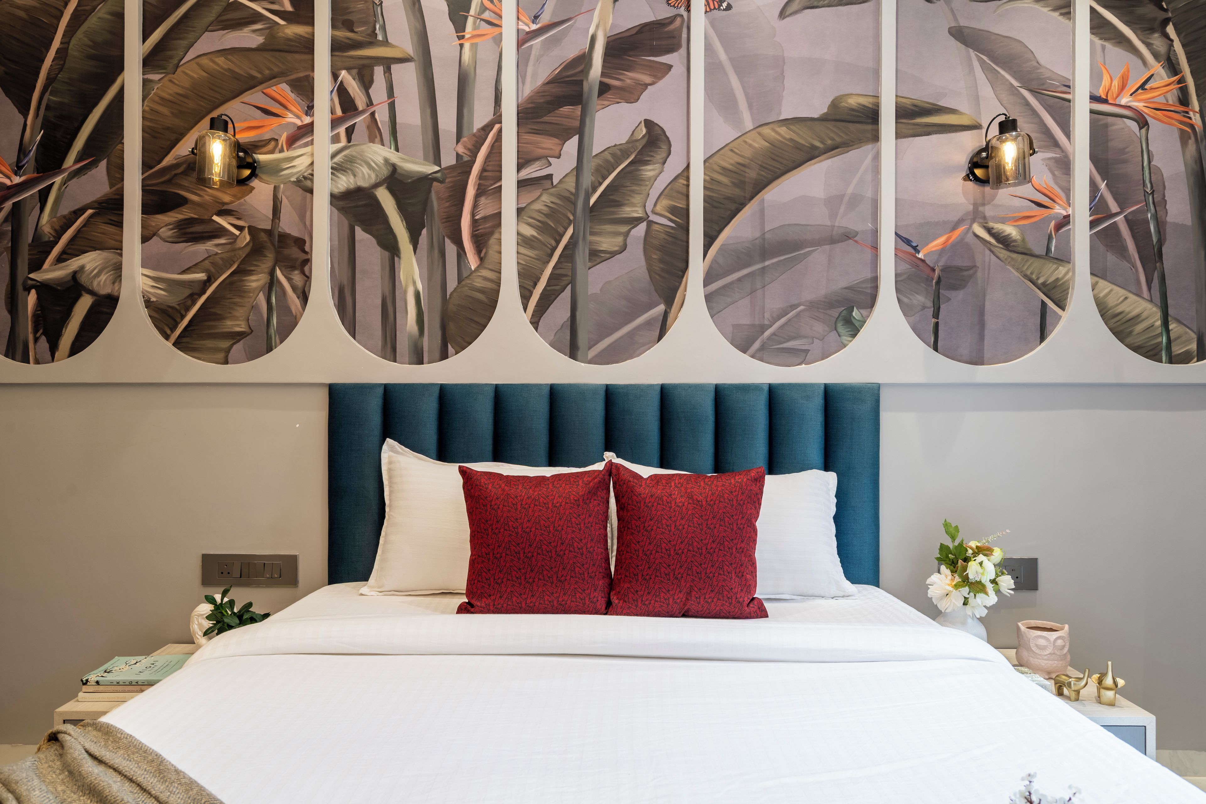 Et hotelværelse med en seng, et blåt sengegavl og en væg med et mural af et tropisk vækstværk.