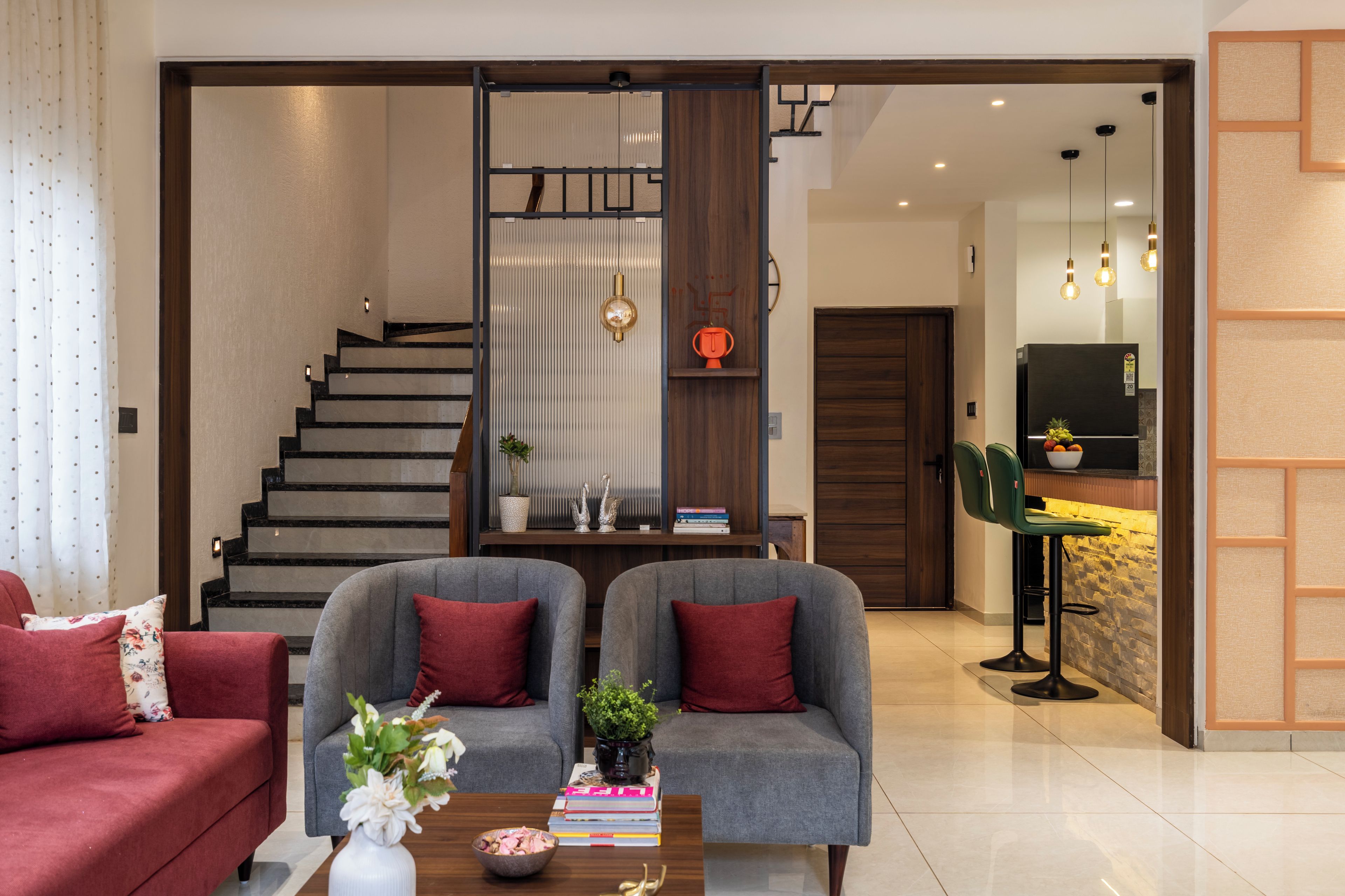 Una sala moderna con un conjunto de sofás, una mesa de centro con objetos decorativos, una estantería y una escalera que conduce a un nivel superior.