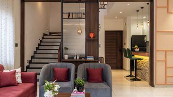 Una sala moderna con un conjunto de sofás, una mesa de centro con objetos decorativos, una estantería y una escalera que conduce a un nivel superior.