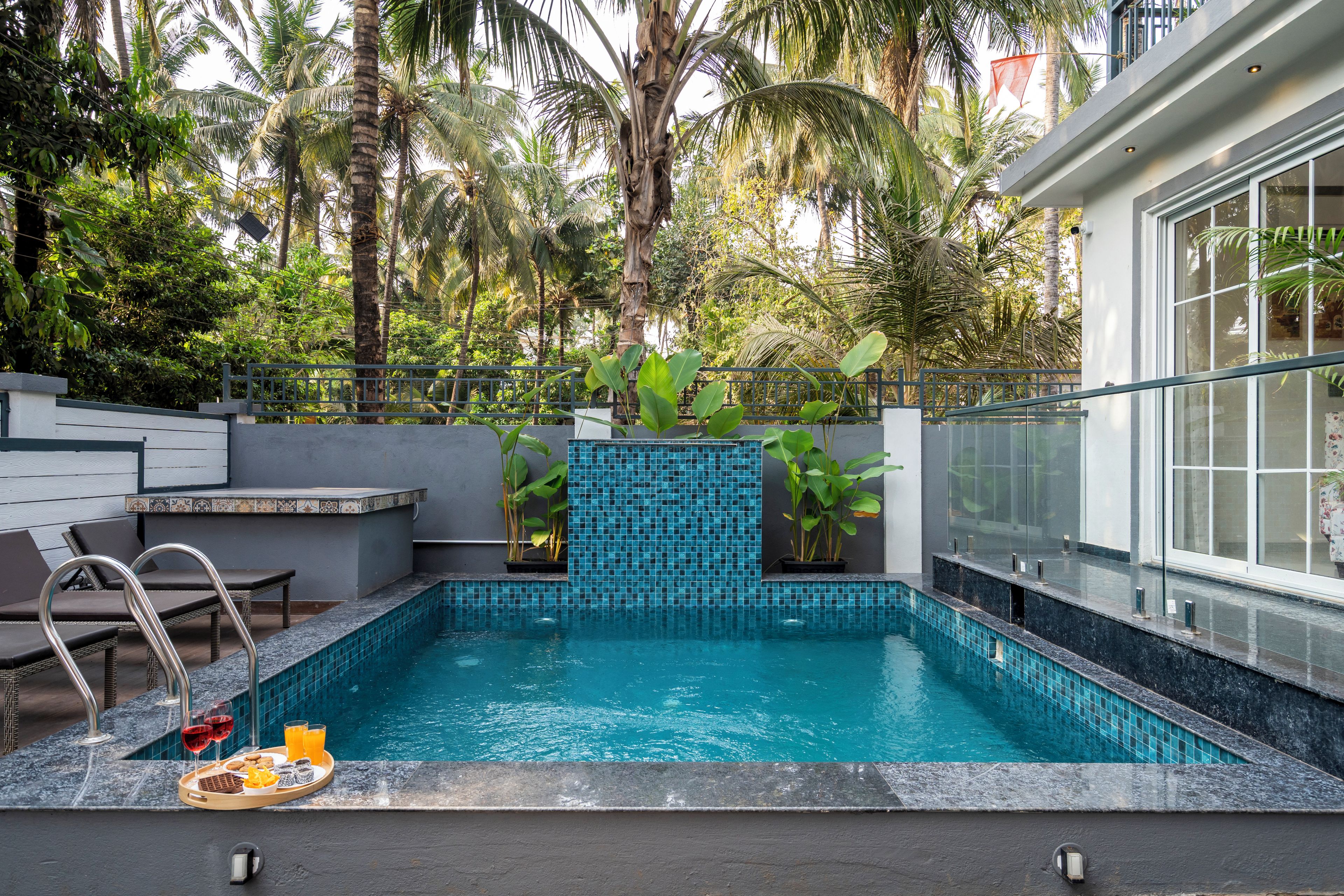 Une piscine avec un mur carrelé, des chaises longues et un plateau avec des boissons et des en-cas.
