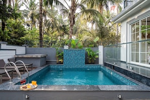 Une piscine avec un mur carrelé, des chaises longues et un plateau avec des boissons et des en-cas.