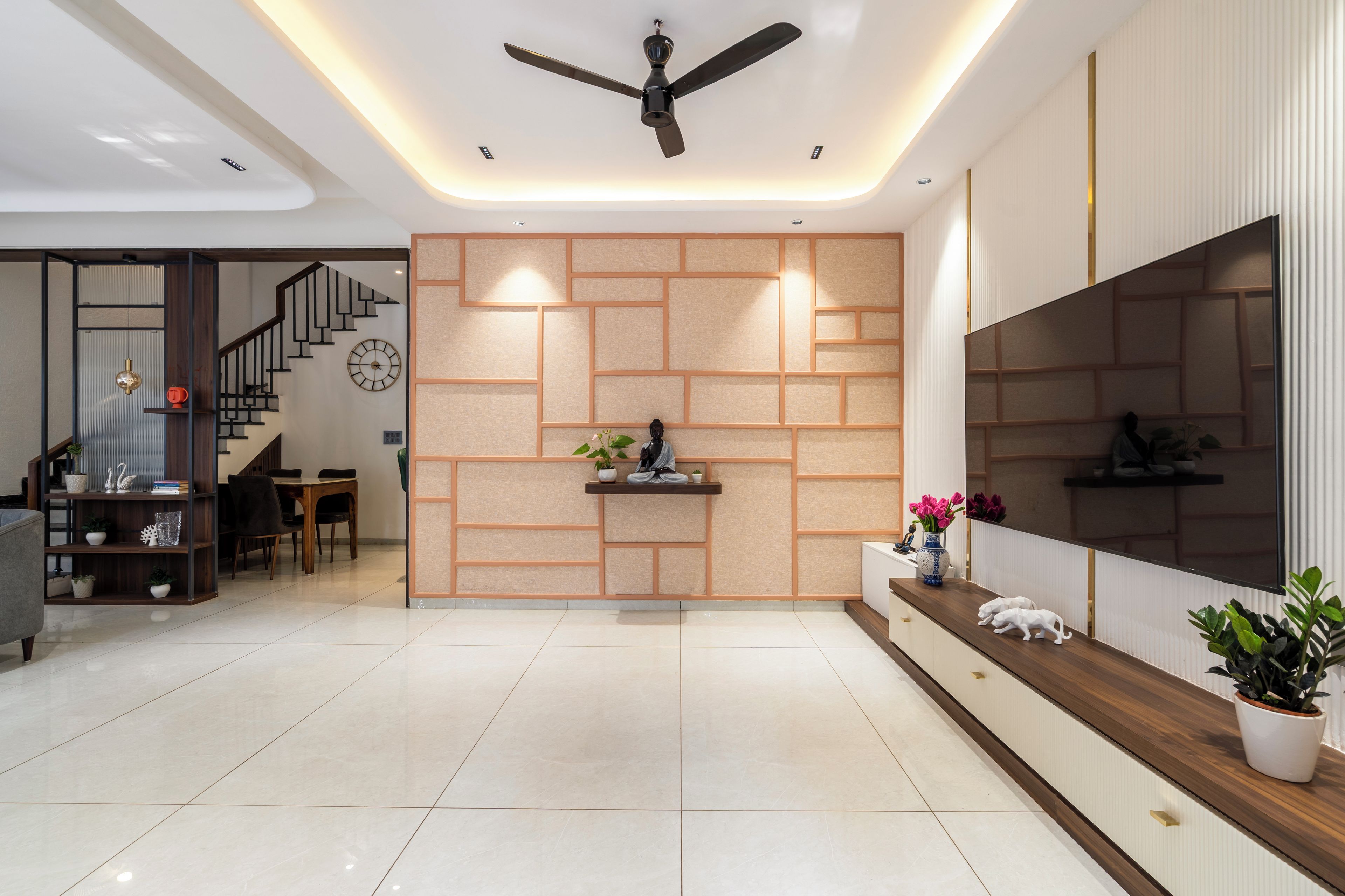 A modern living room with a staircase, a flat-screen TV, and a decorative wall panel.