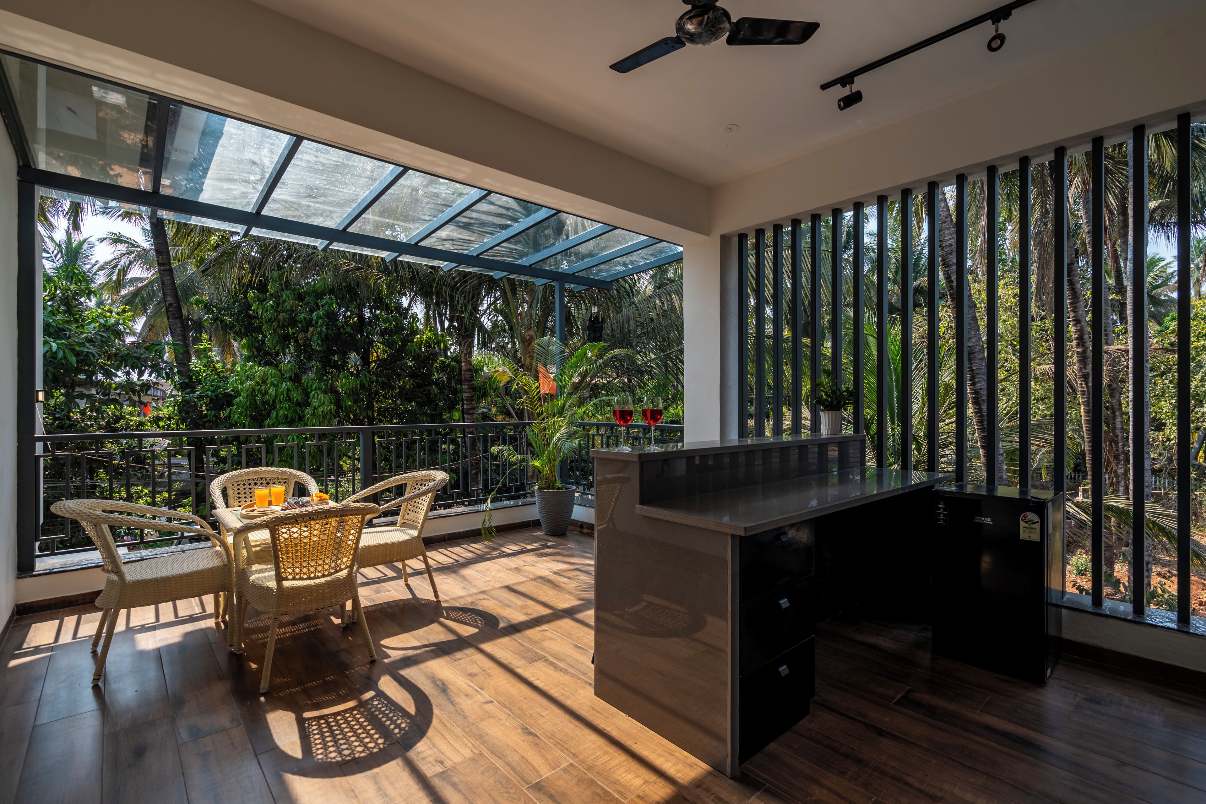 A modern outdoor dining area with a glass-enclosed patio, wicker furniture, and a view of tropical vegetation.