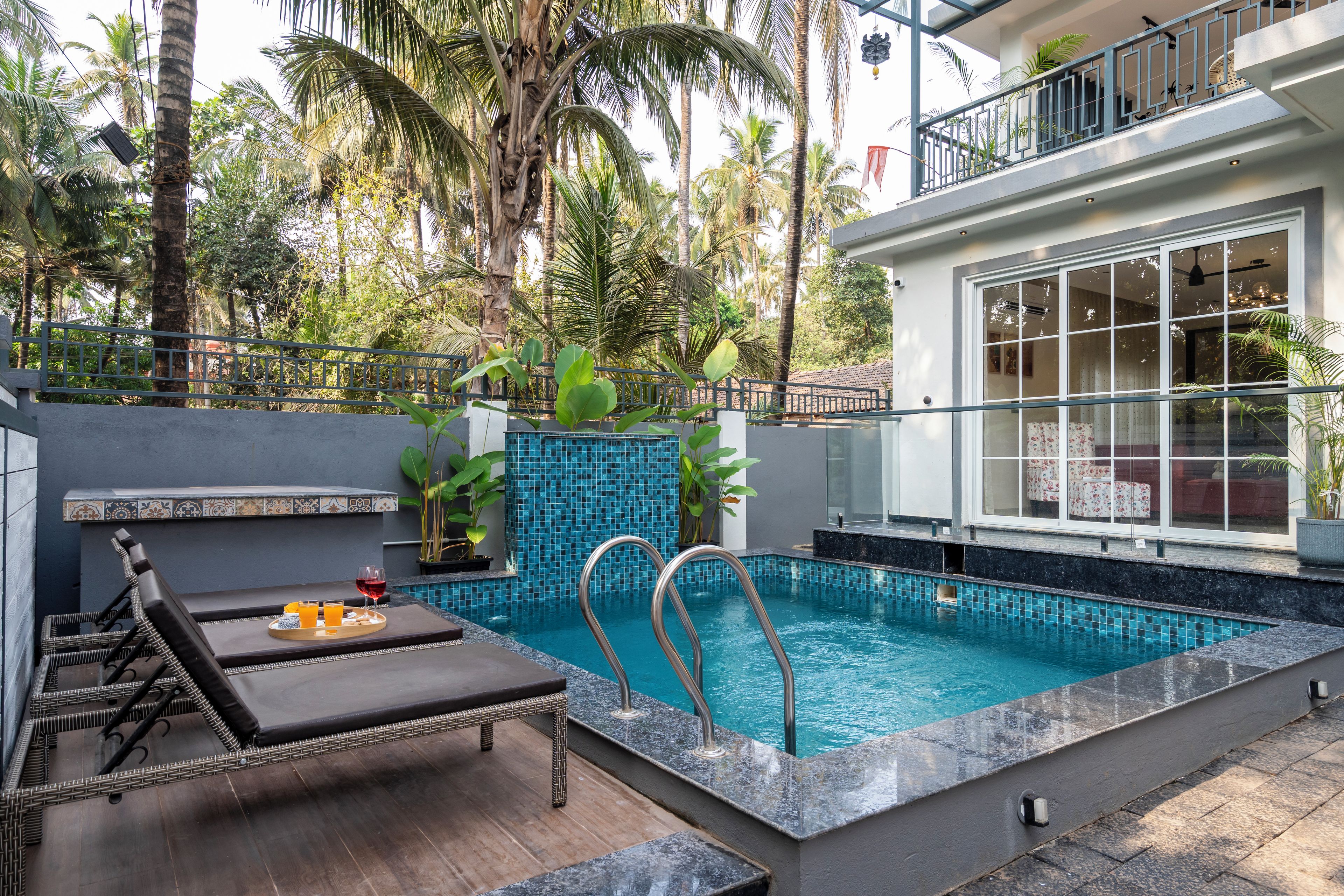 A swimming pool with a tiled edge, lounge chairs, and a dining area with a tray of food and drinks.