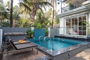 A swimming pool with a tiled edge, lounge chairs, and a dining area with a tray of food and drinks. - Staymaster Aanshal-4BR Villa with Pool (Nerul)