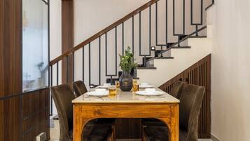A dining area with a wooden table, four chairs, and a vase with flowers. A staircase with a wooden railing is visible in the background.
