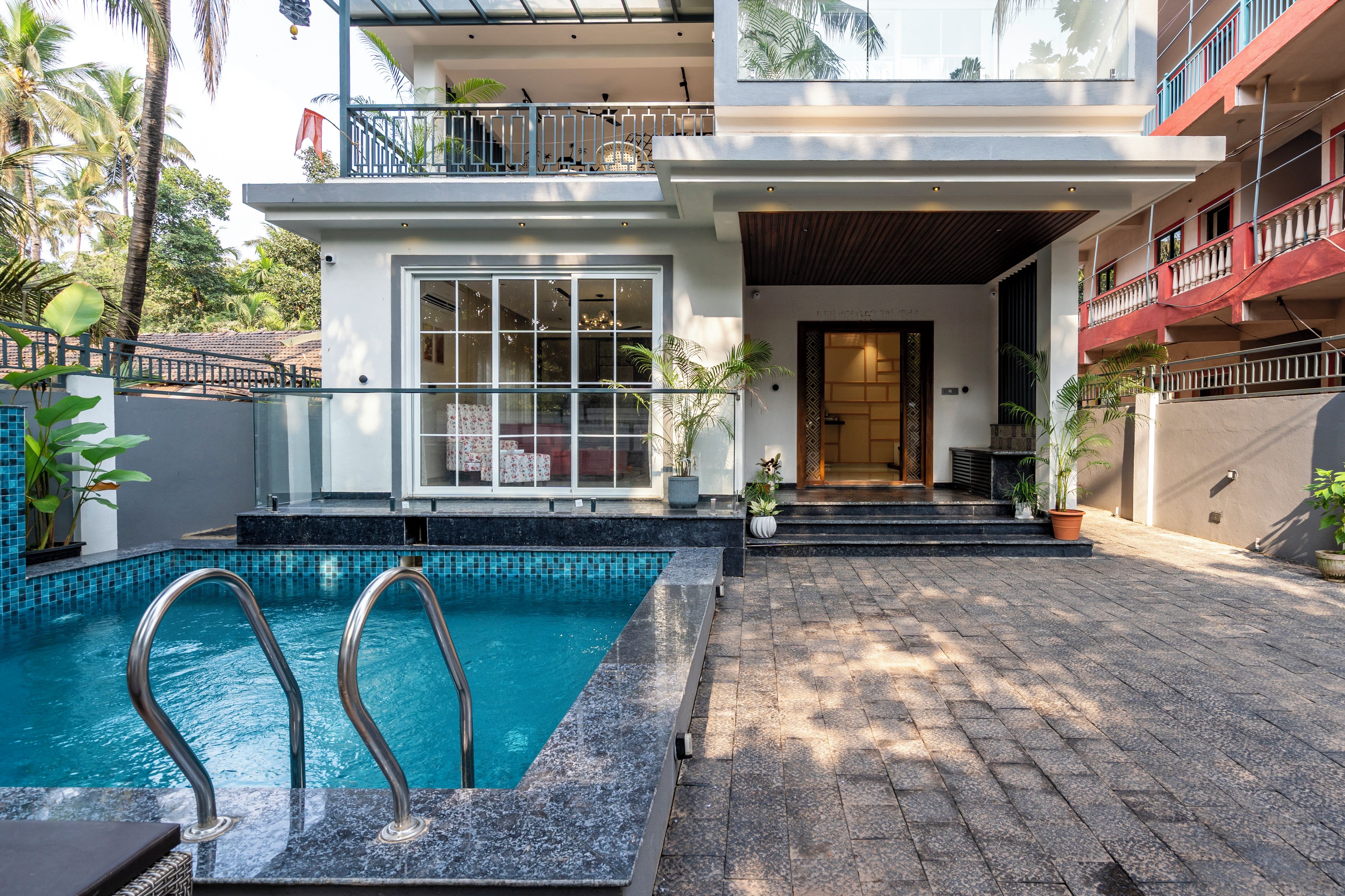 A modern building with a swimming pool, a balcony, and a door leading to the interior.
