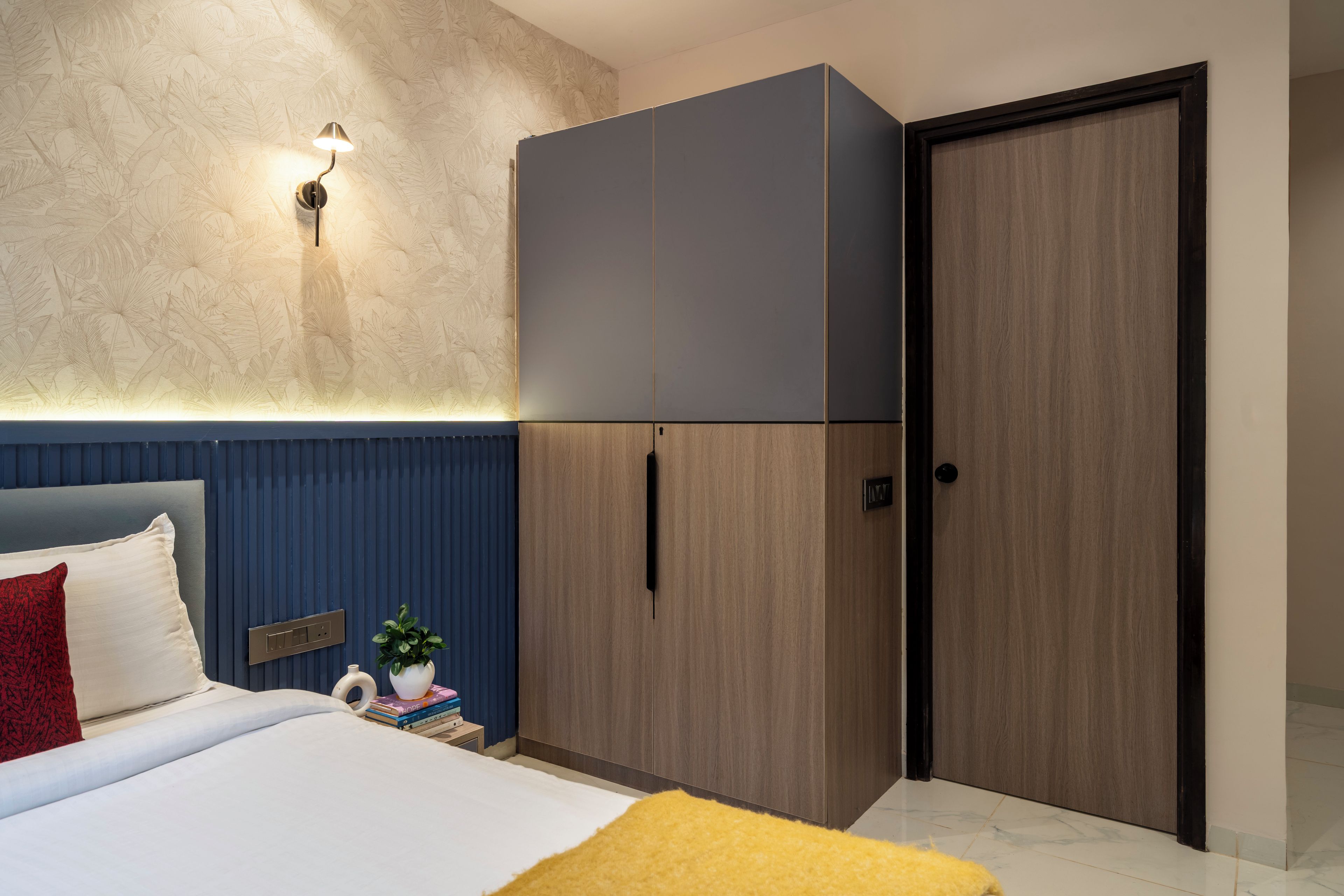 A bedroom with a bed, a wardrobe, a nightstand, a lamp, and a door.